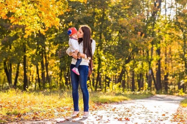 若い母親と彼女の幼児の女の子は秋に楽しんでいます