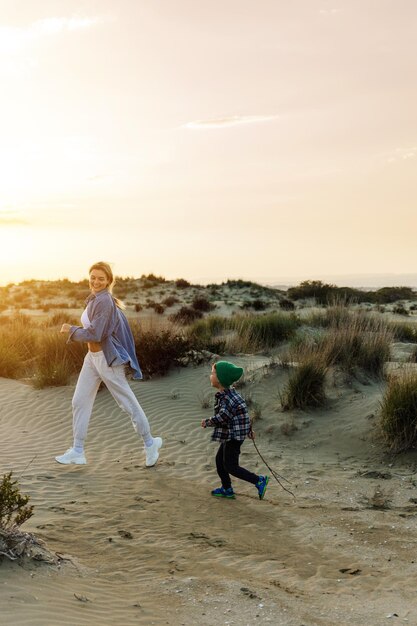 若い母親と幼児の息子が夕暮れ時にビーチで鬼ごっこをする