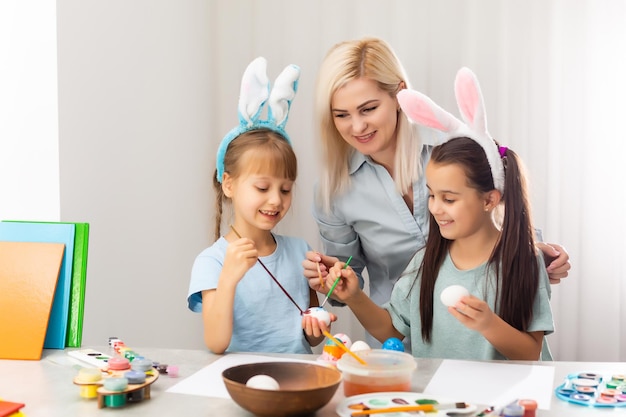 Young mother and her two daughters painting Easter eggs