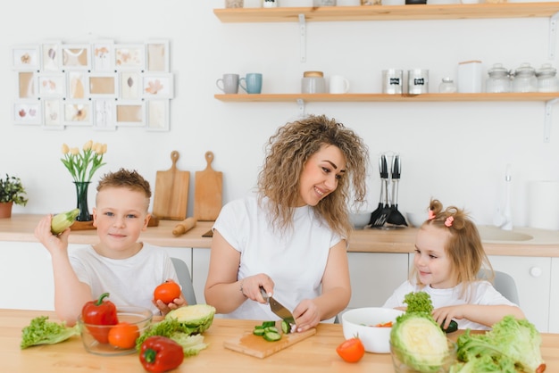 野菜サラダを作る若い母親と彼女の2人の子供