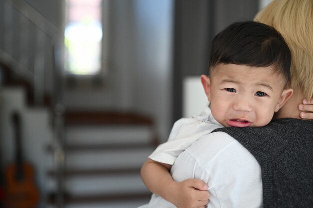 Young mother holding her crying toddler boy and trying to calm him down at home.