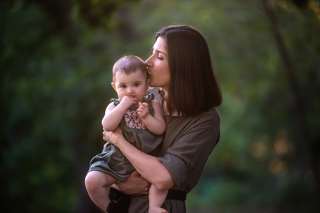 Young mother holds baby in arms in the rays of the sunset in the park.