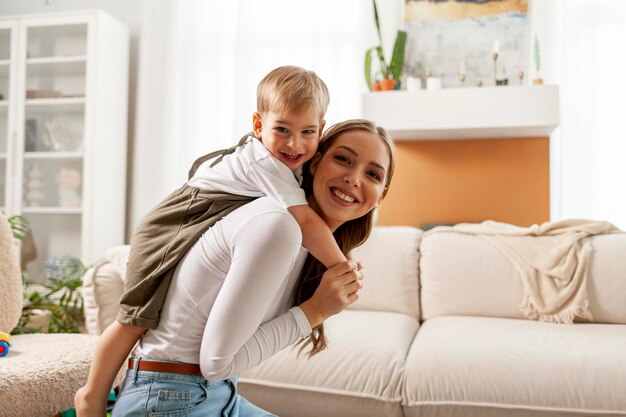 young mother holds her little son on her back and smiles 2yearold boy plays with his parent