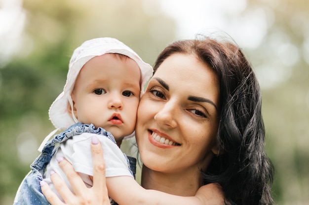 A young mother holds the little daughter of the infante in the park in the summer