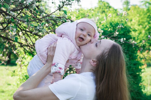 Young mother holds little laughing daughter over nature. Child and parenthood