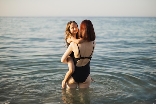 Young mother hugs and holds in her arms her daughter enjoying in beautiful sunny tropical beach