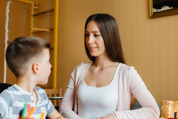 A young mother is doing homework with her son at home. Parents and training