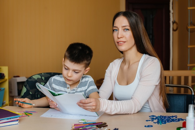 A young mother is doing homework with her son at home. Parents and training