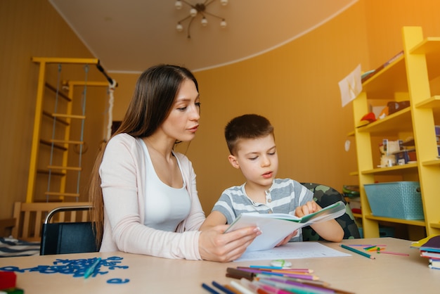 A young mother is doing homework with her son at home. Parents and training.