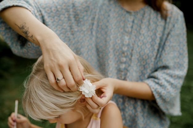 若い母親は庭で彼女の子供の髪を固定しています。家族の時間。