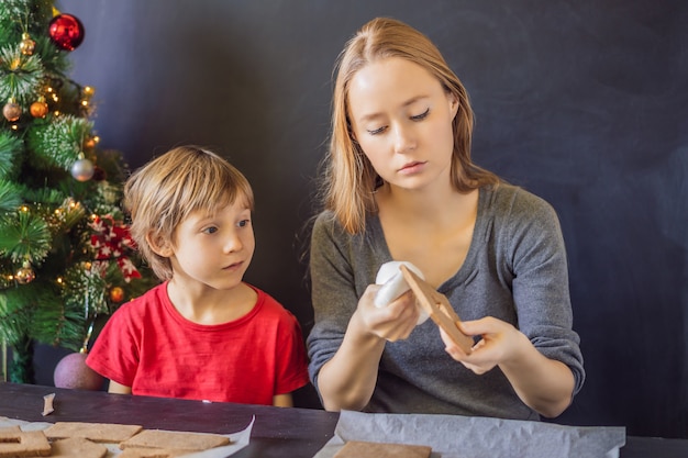 Young mother and kid making gingerbread house