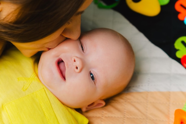 A young mother kisses her adorable newborn baby on the cheek at home The concept of a happy family