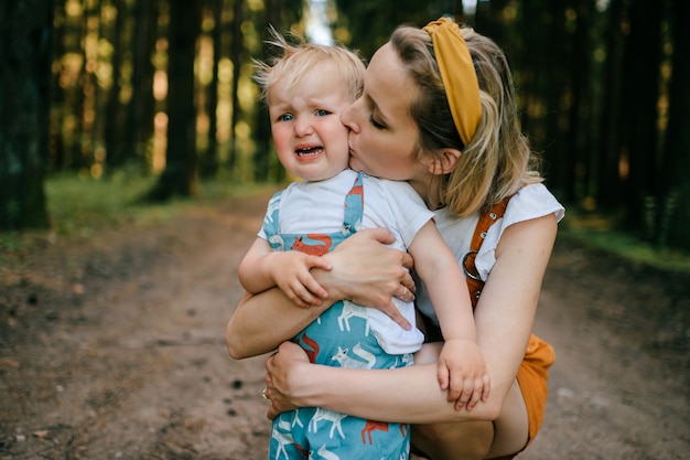 Photo young mother kissing her crying son in the forest