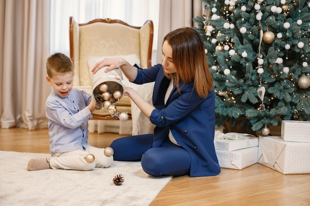 Young mother and little boy sitting near christmas tree at home