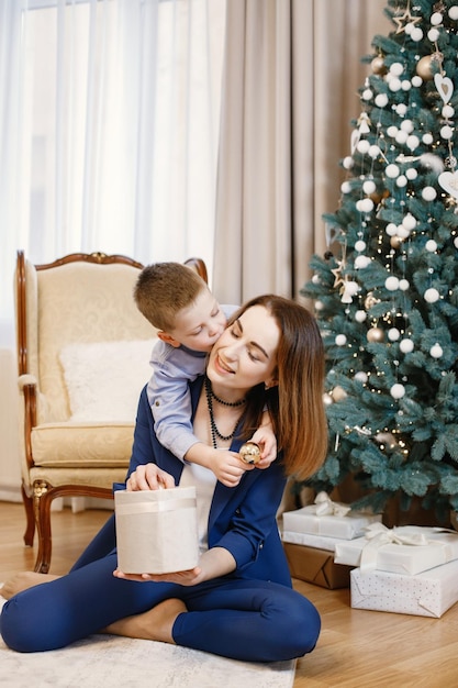 Young mother and little boy sitting near christmas tree at home