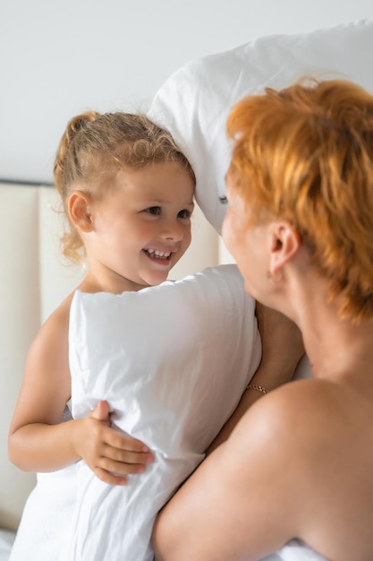 Young mother and little daughter having fun with pillows on bed