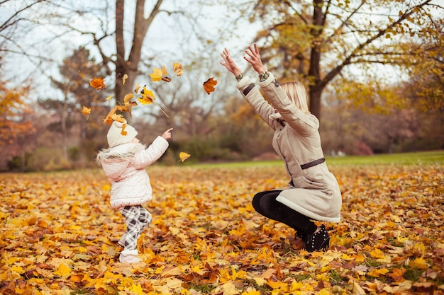 Young mother and little daughter walk in the autumn. Mom and daughter play. Warm winter. Bright autumn. Cozy.