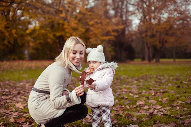 Young mother and little daughter walk in the autumn. Mom and daughter play. Warm winter. Bright autumn. Cozy.