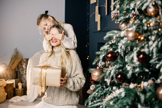 Young mother and little girl sitting near christmas tree at home