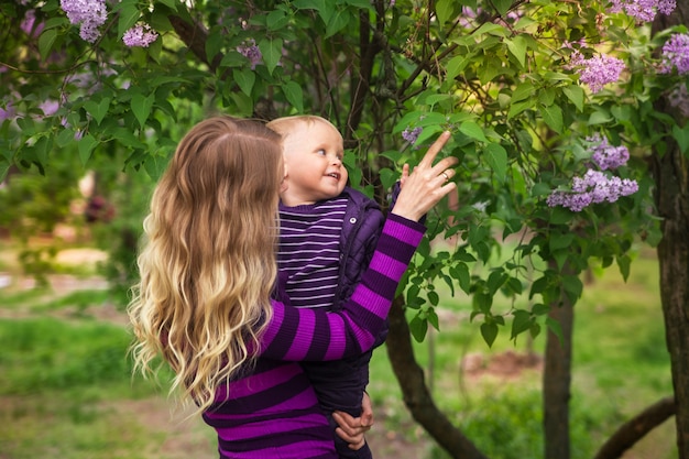 Молодая мать и маленький сын в цветущий сиреневый весенний сад на день матери