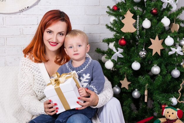 Young mother and little son sitting in front of Christmas tree