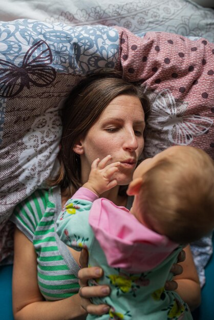 Giovane madre sdraiata sul letto con la sua bambina sdraiata sopra di lei