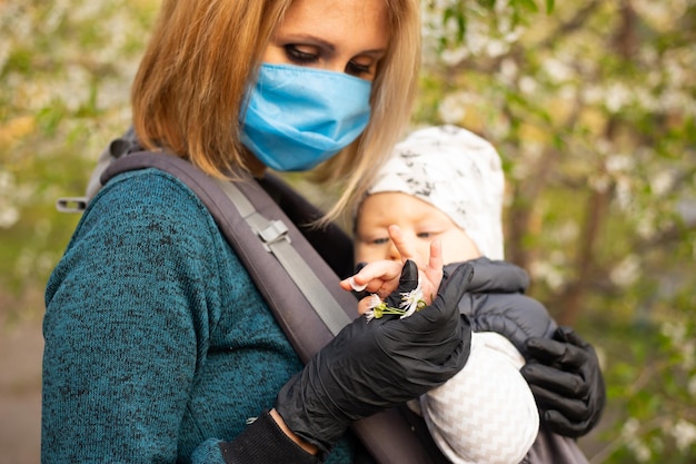 Young mother in medical mask with little son in the park walk near the blooming tree