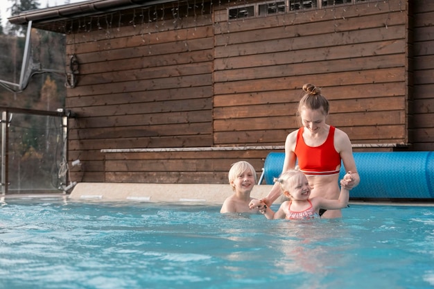 Young mother nanny or sister holding hands of two young children in outdoor pool Holidays with children