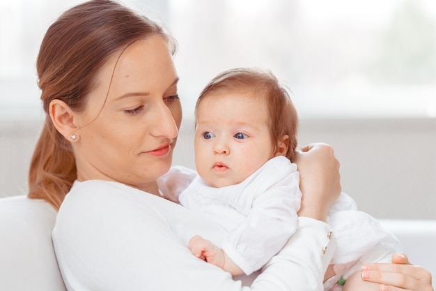 Young mother and newborn baby in white bedroom 