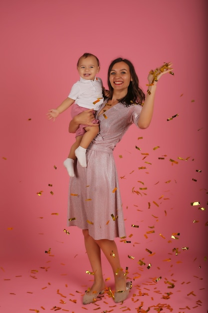 a young mother in a pink dress holds her little son in her arms for a confetti party