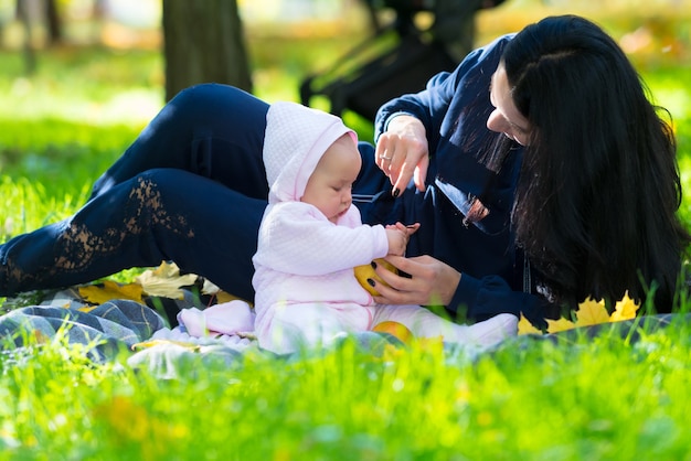 かわいいピンクの衣装で女の赤ちゃんと秋の庭や公園で屋外で遊ぶ若い母親