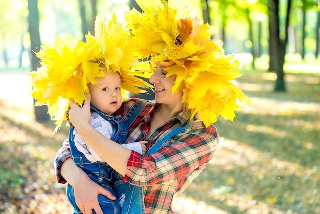 葉の花輪と秋の公園で赤ちゃんと遊ぶ若い母親