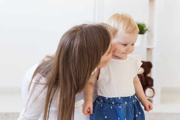 家で女の赤ちゃんと遊んでいる若い母親。母性、幼児および子供の概念。