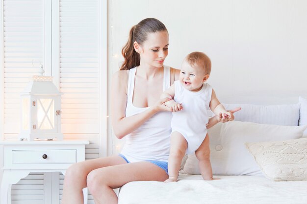 Young mother playing with her cute baby girl in bedroom