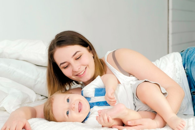 Young mother playing with her little baby on the bed - indoors