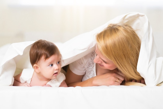 Young mother playing with her newborn child. Mom nursing baby. Happy woman and new born girl relax at home interior. Portrait of happy mother and baby, family at home concept.