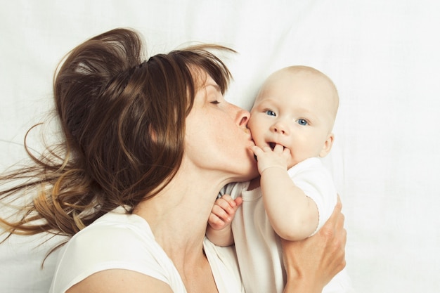 La giovane madre gioca con il suo bambino su un letto con un lenzuolo bianco.