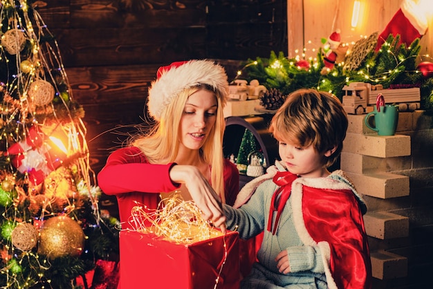 若い母親は、クリスマスに飾られた木と暖炉の近くで息子と遊んでいます。明るい新年
