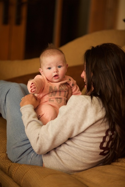young mother plying with cute baby while lying on sofa