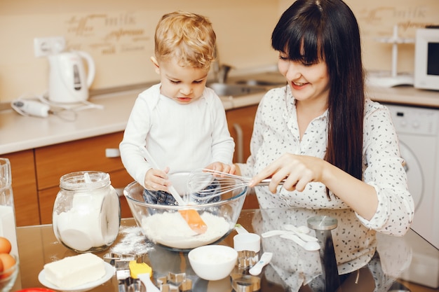 彼女の小さな息子と台所の家で食べ物を準備している若い母