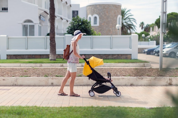 Young mother pushing stroller with sleeping baby outdoors