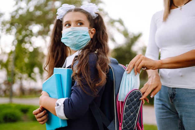 젊은 어머니는 covid19 전염병 동안 여학생의 배낭에 보호용 멸균 마스크를 넣습니다.
