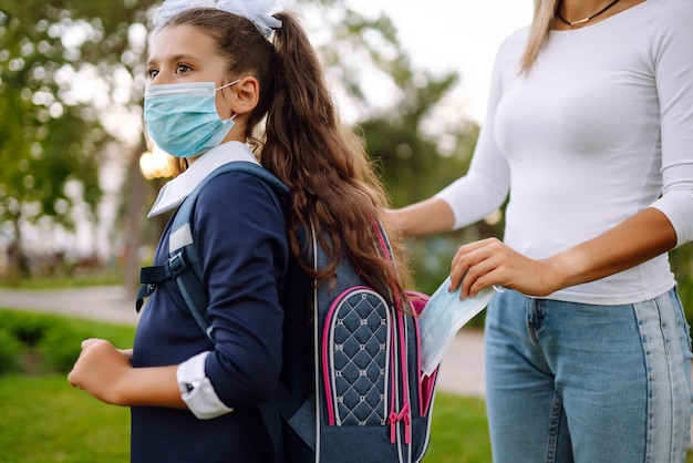 Photo young mother puts a sterile mask in a schoolgirl's backpack. life during covid-19 pandemic.