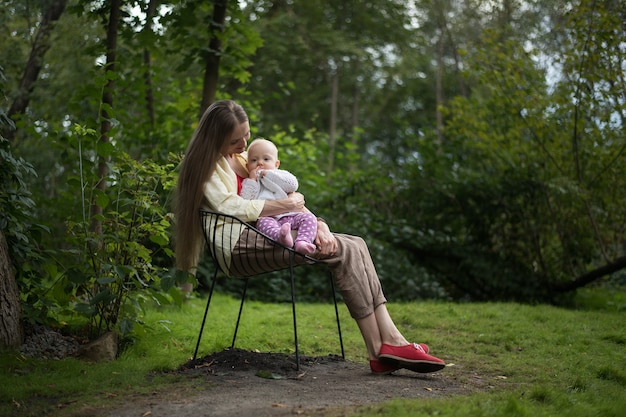 Young mother resting in chair with baby on nature. Stay with child in Park