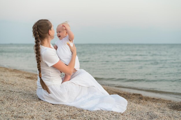 Young mother sitting on beach and holding baby Joys of motherhood