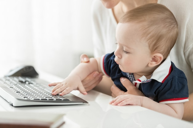 コンピューターの前に座って、膝の上に赤ちゃんを抱いて若い母親
