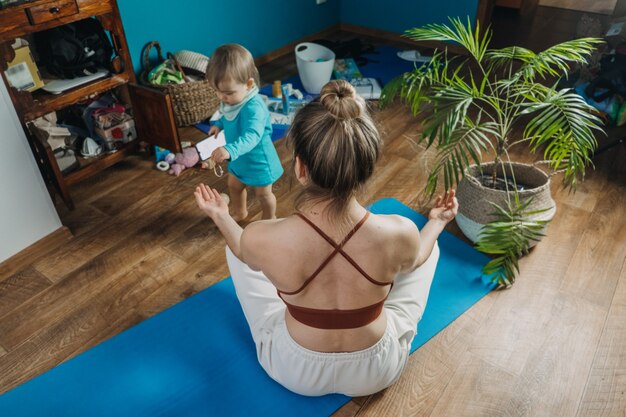 La giovane madre seduta sul pavimento si gode la meditazione e fa esercizi di yoga a casa con la sua piccola figlia