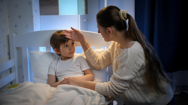 Photo young mother sitting next to her sick little son lying in bed at night concept children illness