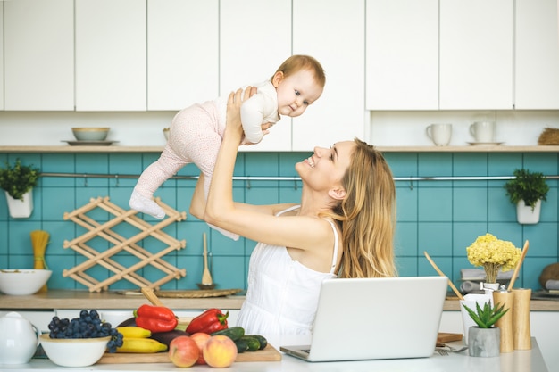 Young mother smiling, cooking and playing with her baby daughter in a modern kitchen. Working at home.