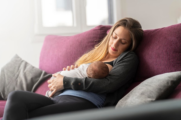 Young mother on the sofa breastfeeding her newborn baby in the living room